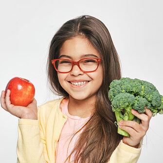 Smiling mixed race girl holding an apple and broccoli in her hands. Healthy vegetarian food for kids